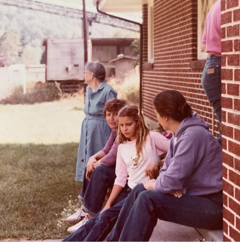 three women sitting on front step, grandmother looks into distance
