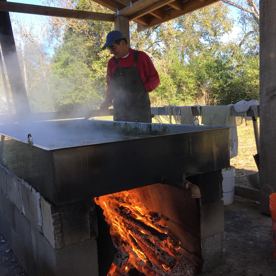 Man stirring sorghum syrup which cooks in pan with blazing fire underneath. 